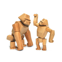 Two wooden gorilla toys. The larger gorilla stands on all four limbs, while the junior gorilla stands on it's rear legs and reaches up towards the larger gorilla's head.