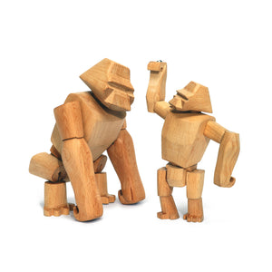 Two wooden gorilla toys. The larger gorilla stands on all four limbs, while the junior gorilla stands on it's rear legs and reaches up towards the larger gorilla's head.