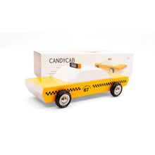 A wooden taxi cab is visible in front of the cars packaging. The cab is yellow and white with black decoration and a taxi sign on the roof.