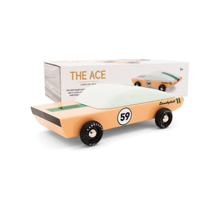 A light brown wooden race car is pictured in front of its packaging. A green racing stripe and number 59 are painted on the car.
