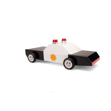 View of the rear of a wooden police car toy. Car is painted white and black with a gold star on the door.