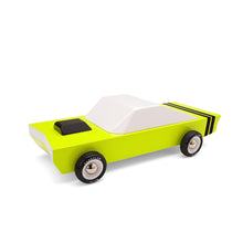 A toy car made from wood. Body is painted bright green-yellow with white windows and black stripes over the trunk.