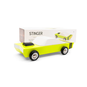 Yellow-green wooden muscle car is visible in front of it's packaging. The car has a black air intake on the hood and black rubber tires.