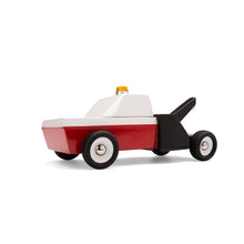 Side view of a toy wooden tow truck. The front is painted red and white, and the back of the truck is black. An orange plastic safety light is attached to the roof.