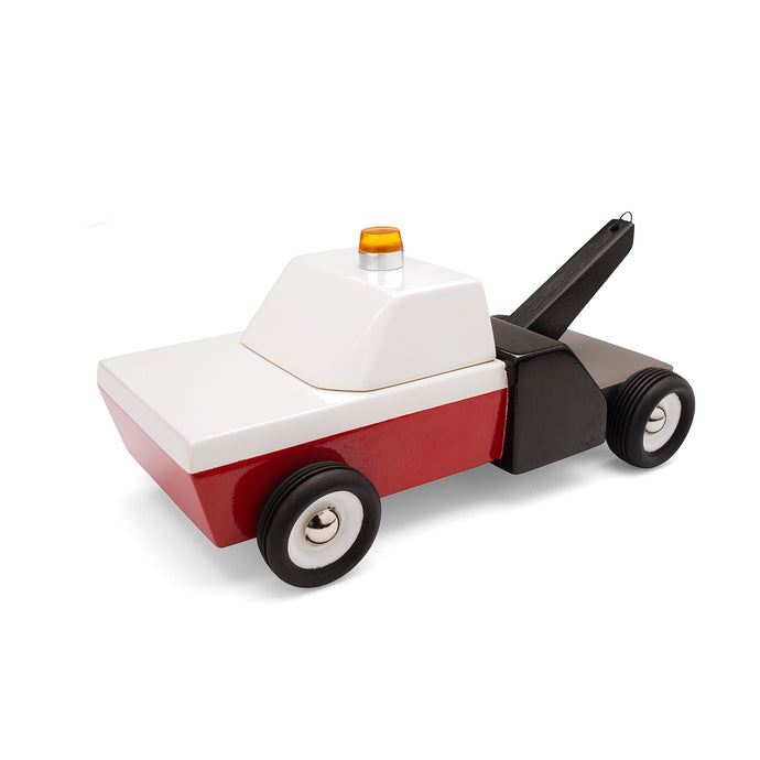 Wooden toy tow truck. The body of the truck is red and white, with a black tail and lift arm. The cab has an orange safety light.