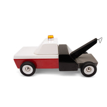Side view of a wooden tow truck. The truck has a red and white front and black rear. The towing arm has a black rubber band that attaches to cars.