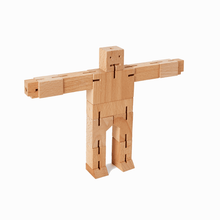 A wooden robot toy stands with his arms spread wide. The robot is made from rectangular blocks of wood with elastic joints.