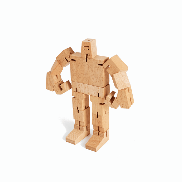 A wooden robot toy stands with both hands on hips. The robot is made from wooden rectangles joined by elastic.