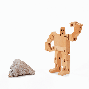 A small wooden robot is shown next to a rock. The robot has one arm raised above it's head.