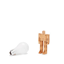 A micro sized wooden robot is pictured next to a light bulb to show scale. The wooden robot is roughly as tall as a traditional incandescent bulb.